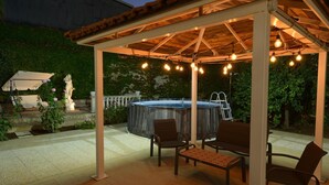 Une terrasse extérieure avec un jacuzzi, des chaises et des guirlandes lumineuses.