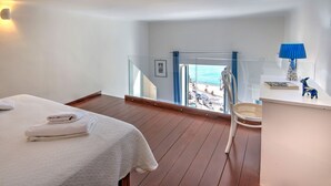 A hotel room with a balcony, a bed with towels, a chair, a lamp, and a view of the beach.