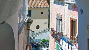 A narrow street with buildings on either side, a balcony with clothes hanging, and a few parked motorcycles.