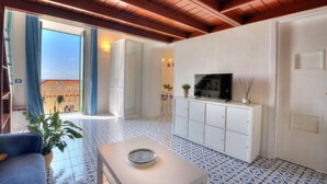 A modern living room with a TV, white cabinets, a blue and white patterned floor, and a balcony with blue curtains.