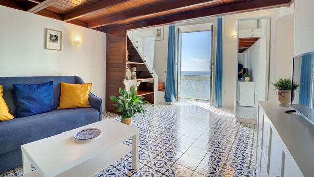 A living room with a sofa, coffee table, and a view of the sea through an open door.