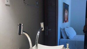 Un baño moderno con un lavamanos grande y rectangular, dos grifos cromados y un dispensador de jabón. Hay dos frascos de vidrio con tapas tejidas en la encimera.