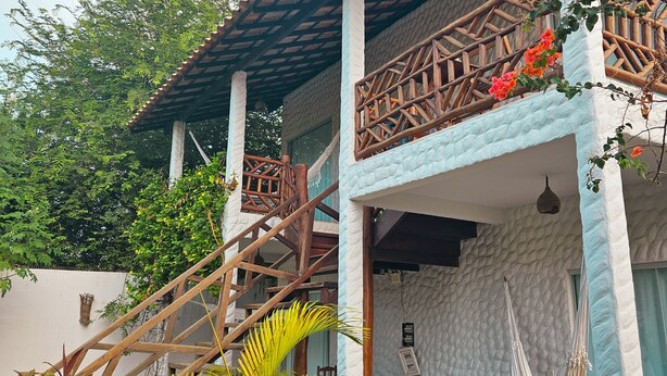 Una escalera de madera tradicional que conduce a un espacio exterior cubierto con una hamaca y sillas de madera.