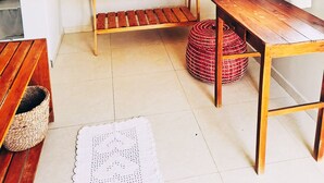 Una habitación con estructura de cama de madera, una pequeña mesa de madera, una cesta tejida y un taburete redondo tejido.
