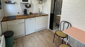 A compact kitchen with white cabinets, a microwave, and a sink. There's a dining table with two chairs and a small trash bin. - T2 Plein Centre D'arcachon au Calme. Animaux Acceptés (Arcachon)