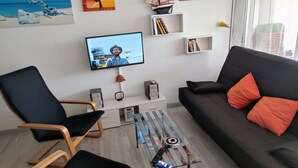 En moderne stue med en sort sofa, orange puder, et sofabord i glas og et fjernsyn monteret på væggen.