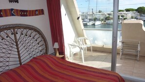 En balkon med seng, stol og udsigt til både og bygninger.