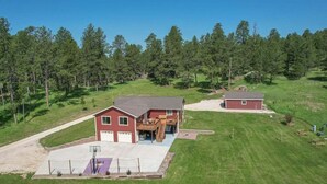 A two-story house with a garage, a basketball court, and a large yard surrounded by trees. - Custer Connection- Private Retreat: 6-Acre Nature Escape with Trail Access, Custer. (Custer)