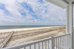 A beach view from a balcony with a wooden deck and a white railing.