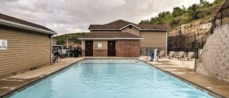 A swimming pool with a building in the background, a covered area, and a stone wall.