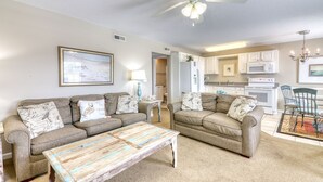 A living room with two sofas, a coffee table, a ceiling fan, and a kitchen in the background. - Oceanfront Blockade Runner Villa - Pool (North Myrtle Beach)