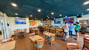 A restaurant with wooden tables and chairs, a bar area, and a kitchen in the background. - Oceanfront Blockade Runner Villa - Pool (North Myrtle Beach)