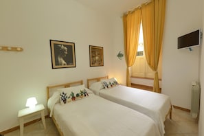 A hotel room with two beds, a nightstand, a lamp, a flat-screen TV, and a window with curtains. - Vacation home with private pool, Floridia (Floridia)