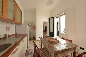 A compact kitchen with wooden cabinets, a stainless steel sink, and a refrigerator. A dining table with chairs is set up in the adjacent room. - Vacation home with private pool, Floridia (Floridia)