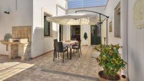 Un patio con una mesa, sillas, una sombrilla blanca y una planta en maceta.