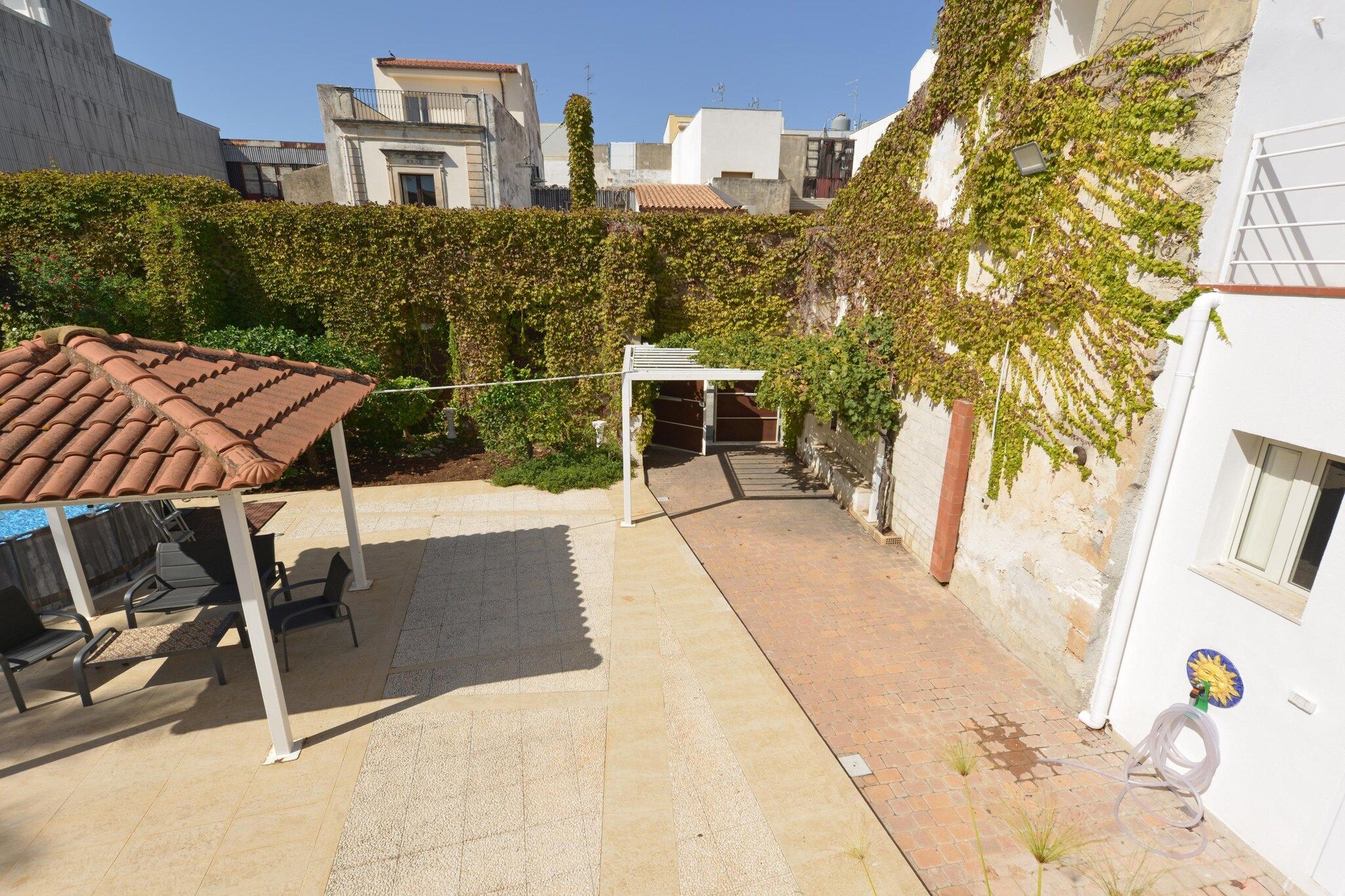 A courtyard with a pergola, outdoor seating, and a white building with ivy.