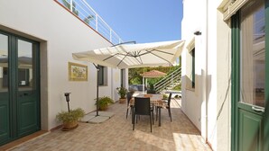 Un patio con mesa y sillas, una zona cubierta y plantas en macetas.