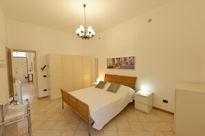 A bedroom with a bed, nightstands, a wardrobe, a chandelier, and a painting on the wall.