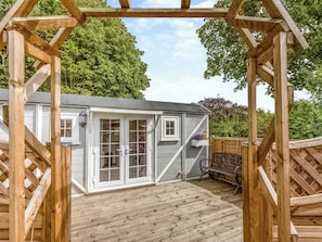 A wooden deck with a pergola structure, a small shed with glass doors, and a bench.