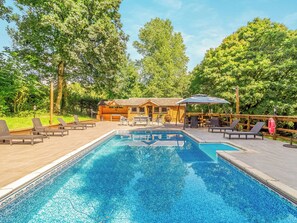 A pool area with lounge chairs, a wooden deck, and a building with a covered patio.