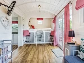 A compact, well-lit room with a bunk bed, a small kitchenette, and a window with red curtains.
