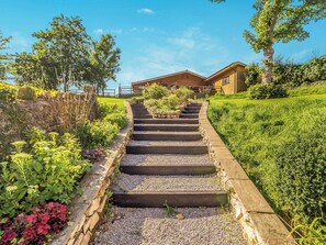 A staircase leading to a wooden building with a stone border, surrounded by greenery and a clear sky.