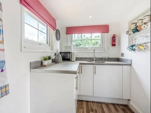 A compact kitchen with white cabinets, a microwave, a sink, and a window with red valance.