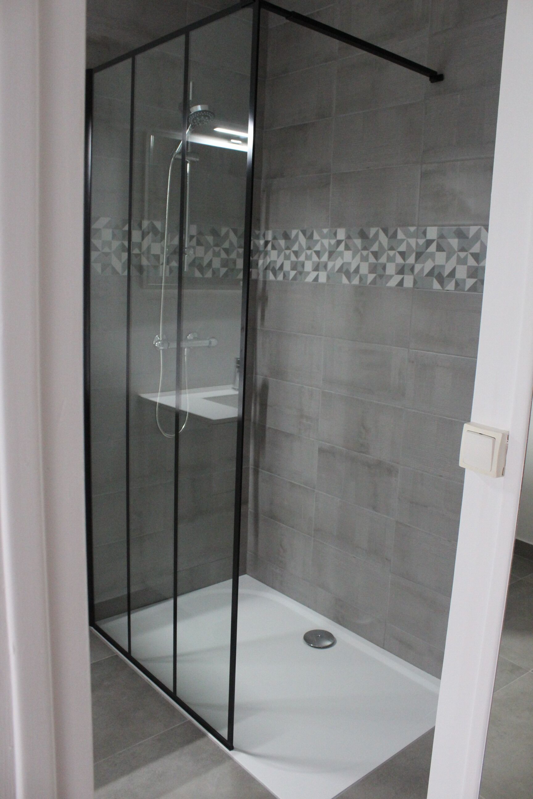 A glass-enclosed shower area with a white sink and a tiled floor.