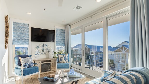 A spacious living room with a large window, a flat-screen TV, and a cozy seating area with a sofa and armchairs. - Golf Cart Boardwalk to the Beach, Resort Pools (Port Aransas)