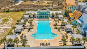 A resort with a central swimming pool, multiple lounge areas, and a view of the ocean. - Golf Cart Boardwalk to the Beach, Resort Pools (Port Aransas)