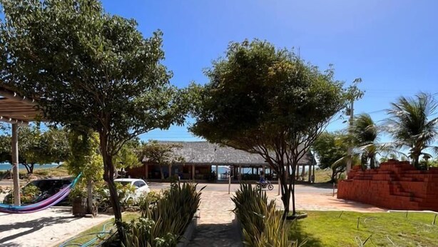 A stone pathway leading to a thatched-roof structure surrounded by potted plants and trees. - Pousada e Restaurante do Francisco (Icapuí)