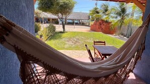 A hammock in a covered outdoor area with a view of a courtyard and palm trees. - Pousada e Restaurante do Francisco (Icapuí)