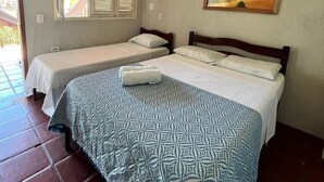 A hotel room with two single beds, a large bed with a patterned bedspread, a painting of a beach scene, and an air conditioning unit on the wall. - Pousada e Restaurante do Francisco (Icapuí)