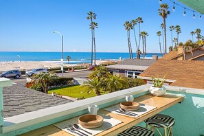 Terraza en la azotea con mesa lista para comer, con vistas a una playa con palmeras y un cielo azul despejado.