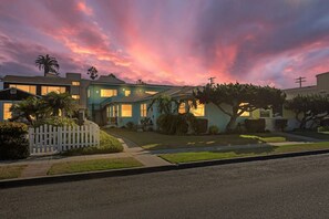 Una calle residencial con casas, una cerca blanca de piquetes y un árbol.
