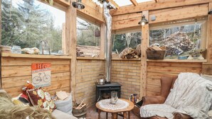 A cozy cabin interior with a wood-burning stove, a cushioned chair, and a small table. - The Cottage In The Woods (Taynuilt)