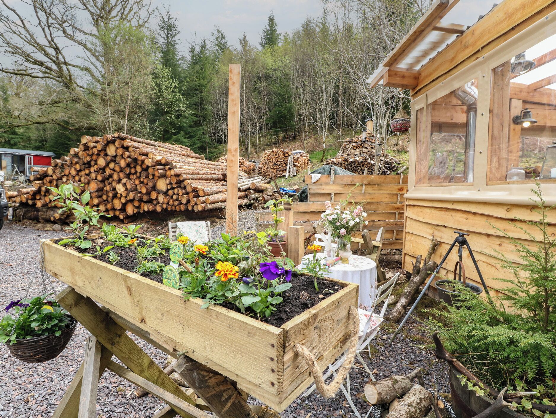 A rustic wooden cabin with a garden bed filled with various plants and flowers.