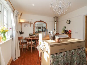 A kitchen with wooden cabinets, a dining table, chairs, a coffee maker, and a fruit bowl. - The Cottage In The Woods (Taynuilt)