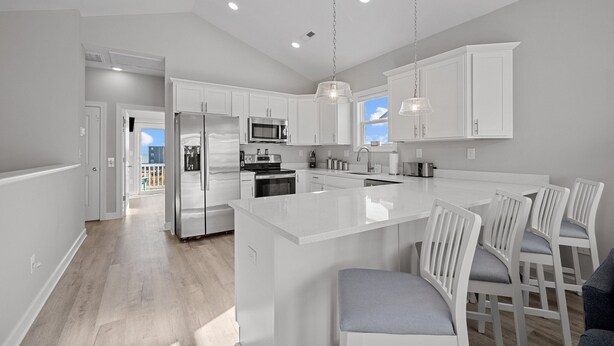 Una cocina moderna con armarios blancos, electrodomésticos de acero inoxidable y una isla central con taburetes de bar.
