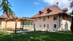 A two-story house with a red-tiled roof, a wooden pergola, and a grassy yard. - Maison Indépendante en Chartreuse (Saint-Laurent-du-Pont)