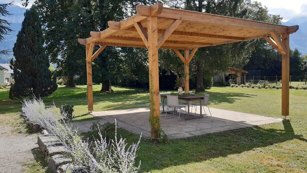 A wooden pergola with a table and chairs underneath, surrounded by a grassy area and trees. - Maison Indépendante en Chartreuse (Saint-Laurent-du-Pont)