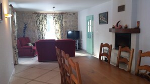 A living room with a red sofa, a television, a fireplace, and a dining area with wooden chairs. - Maison Indépendante en Chartreuse (Saint-Laurent-du-Pont)