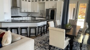 Eine moderne Küche mit weißen Schränken, einer zentralen Kochinsel und einem Essbereich mit einem dunklen Holztisch und passenden Stühlen.