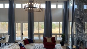 Ein geräumiges Wohnzimmer mit großem Fenster, Kamin und einer Kristallleuchtre.'