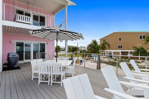 A deck with a table and chairs, a covered grill, and a view of the beach and ocean. - Pinkies Up: Stunning MB Home- 4BR, Beachfront, Private Pool, Pet Friendly, Amazi (Mexico Beach)