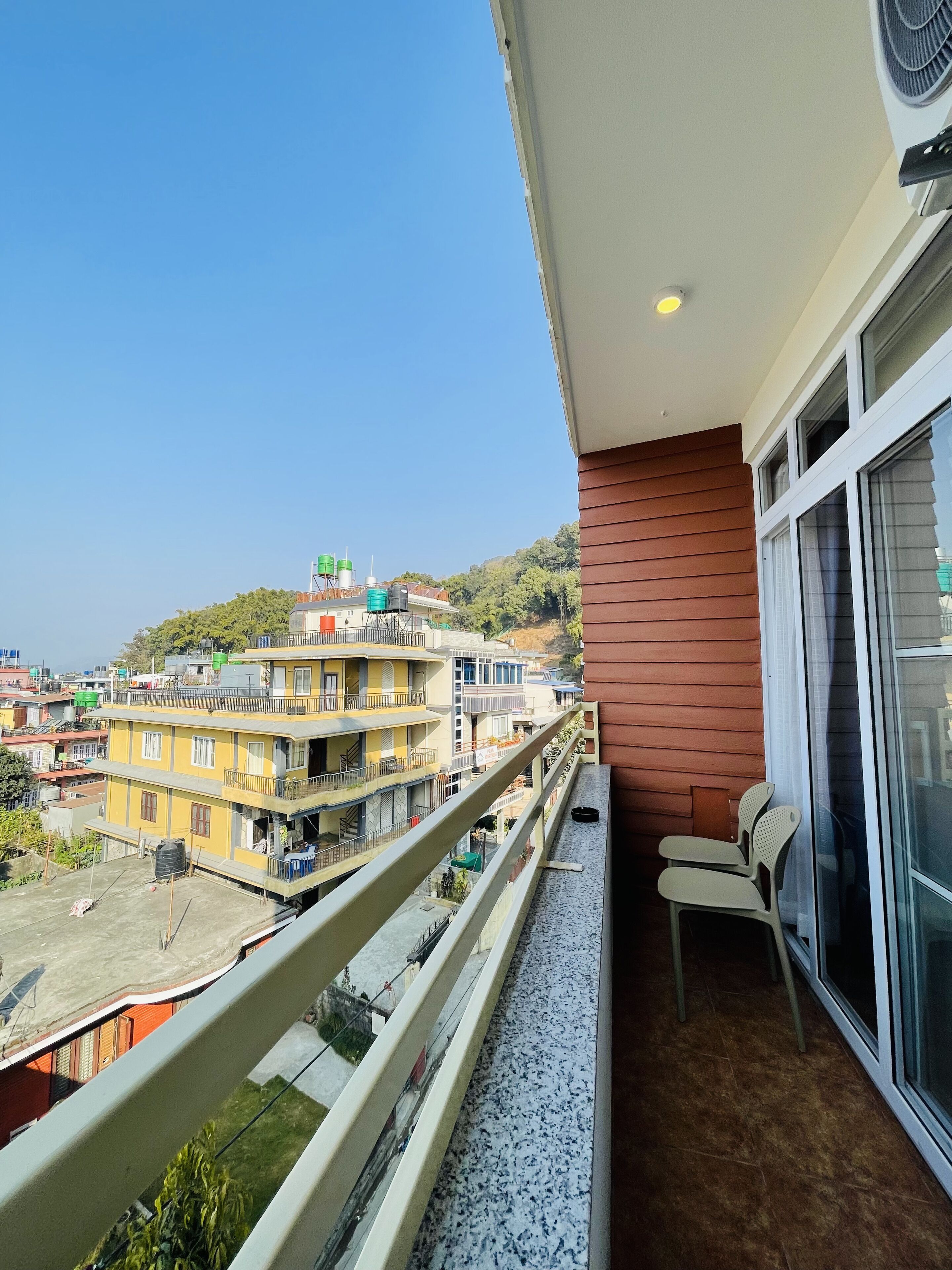 A balcony with a view of a residential area, a chair, and a window with a curtain.