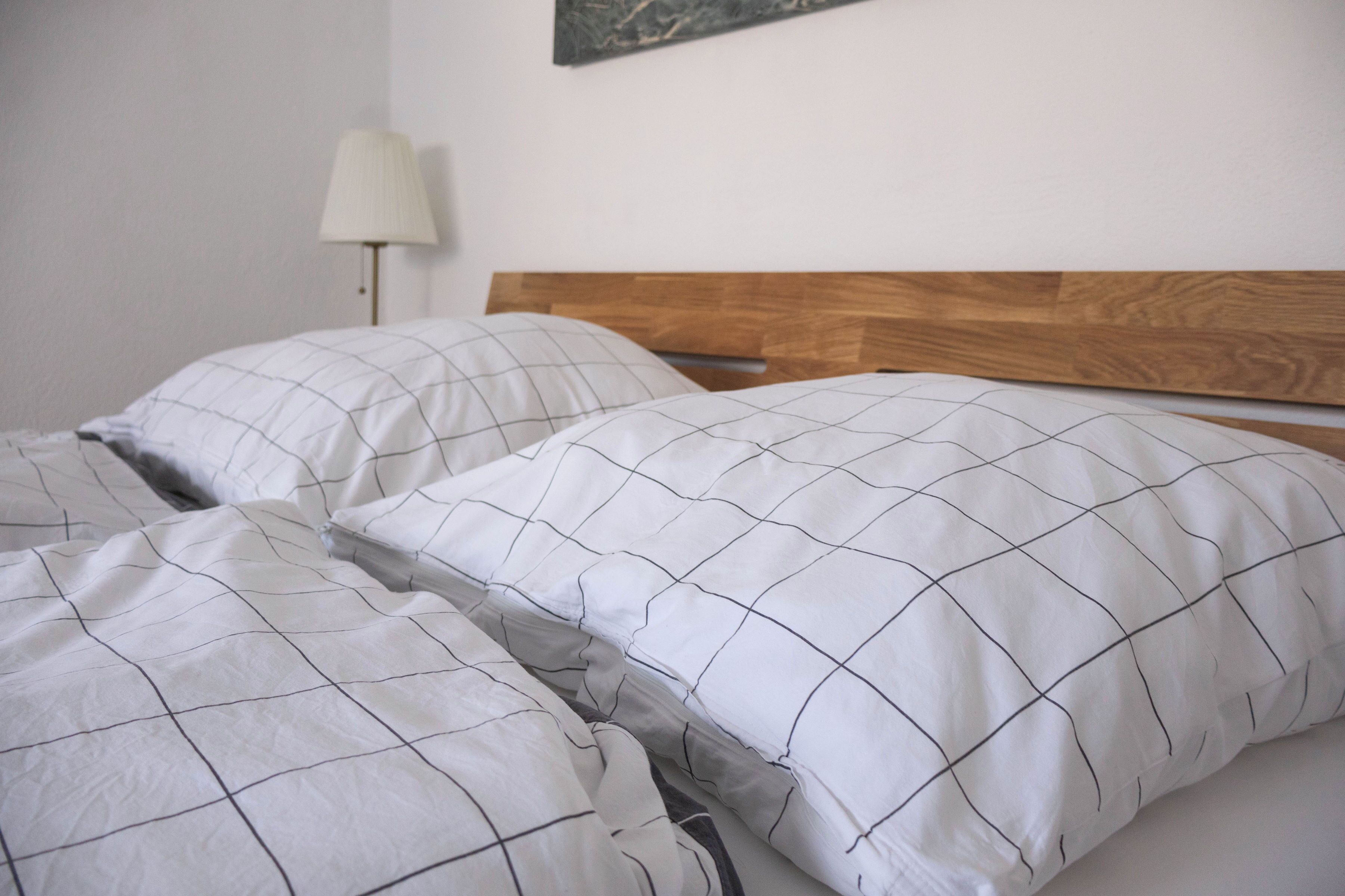 A bed with a wooden headboard and white bedding with a grid pattern.