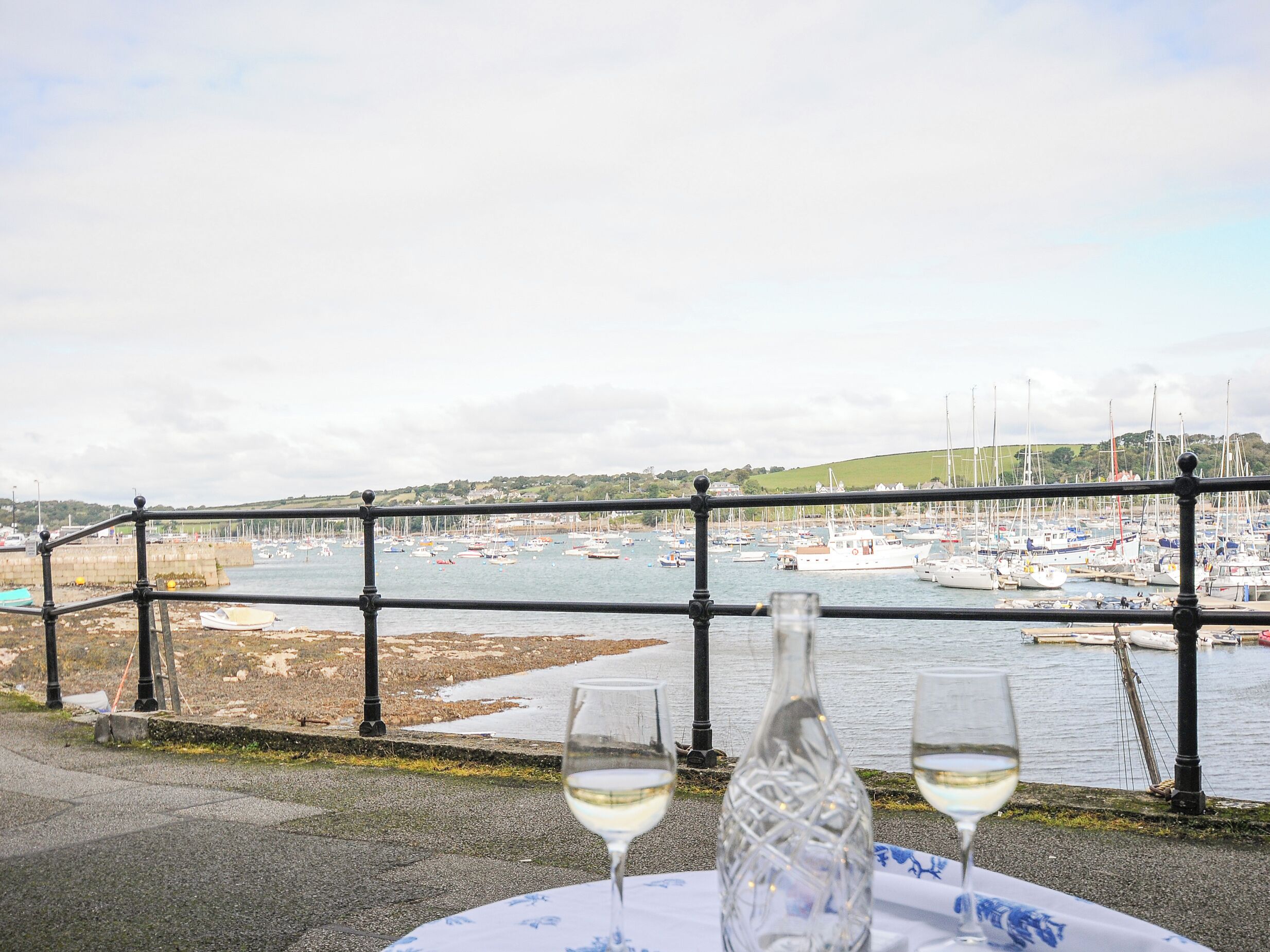 A table with two wine glasses and a bottle, overlooking a marina with boats.