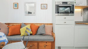 A compact living space with a wooden sofa, a small kitchen area including a stove and oven, and a mirror on the wall. - Zawn Nook (Falmouth)