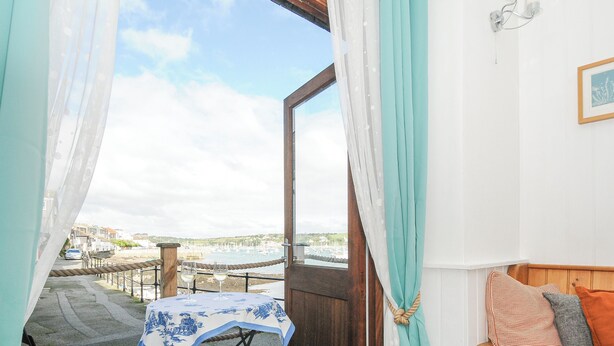 A balcony with a table covered by a blue and white tablecloth, a chair, and a sofa with cushions. - Zawn Nook (Falmouth)